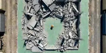 Economic Crossroads: Avoiding Common Pitfalls in Modern Market Shifts Aerial view of a construction worker inspecting a crack in a vast green concrete foundation, surrounded by fragmented geometric patterns of a partially demolished building, symbolizing overlooked systemic economic risks.